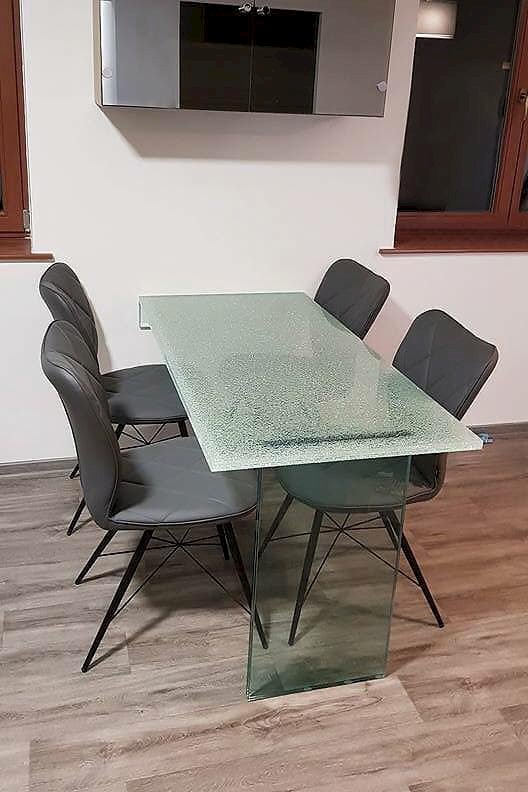 Skleněný jídelní stůl s deskou s dekorem crash glass a čtyřmi šedými židlemi na parketové podlaze