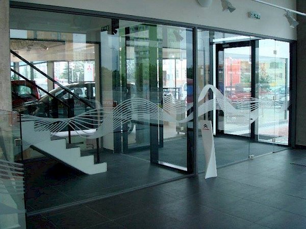Skleněné zástěny v autosalonu s abstraktním vzorem, průhled na schodiště a auta