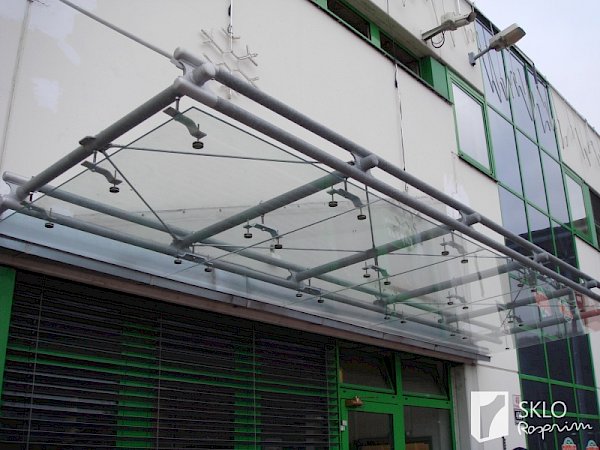 Podlouhlá skleněná stříška v industriálním stylu nad vchodem do obchodu